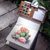 A portable wooden watercolor paint set with a palette and a watercolor painting of a pink cactus on a white background.