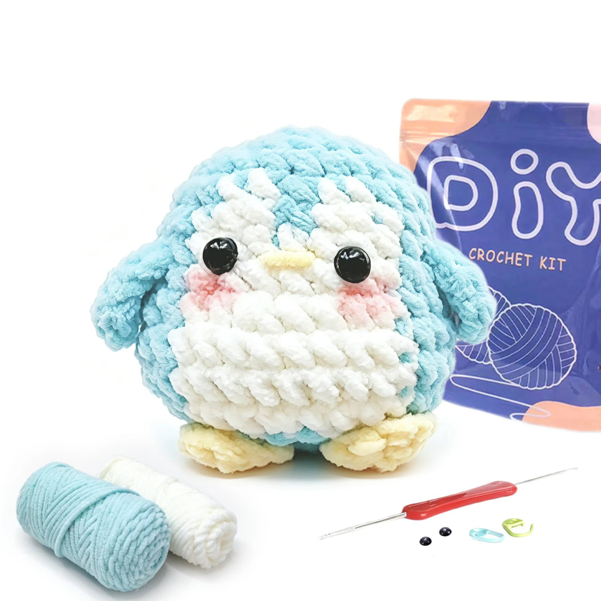 A crocheted blue and white owl toy next to yarn, needles, and small craft items for a beginner crochet kit.