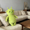 A bright lime green alien cat plush toy sitting on a light beige sofa.