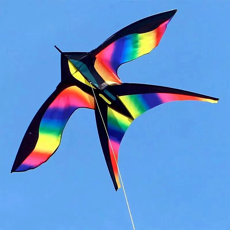 A colorful rainbow nylon kite is flying against a clear blue sky.