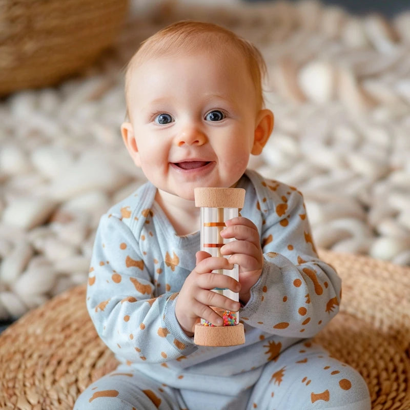 Un bébé souriant tenant un rattle éducatif en bâton arc-en-ciel en bois sur un fond clair.