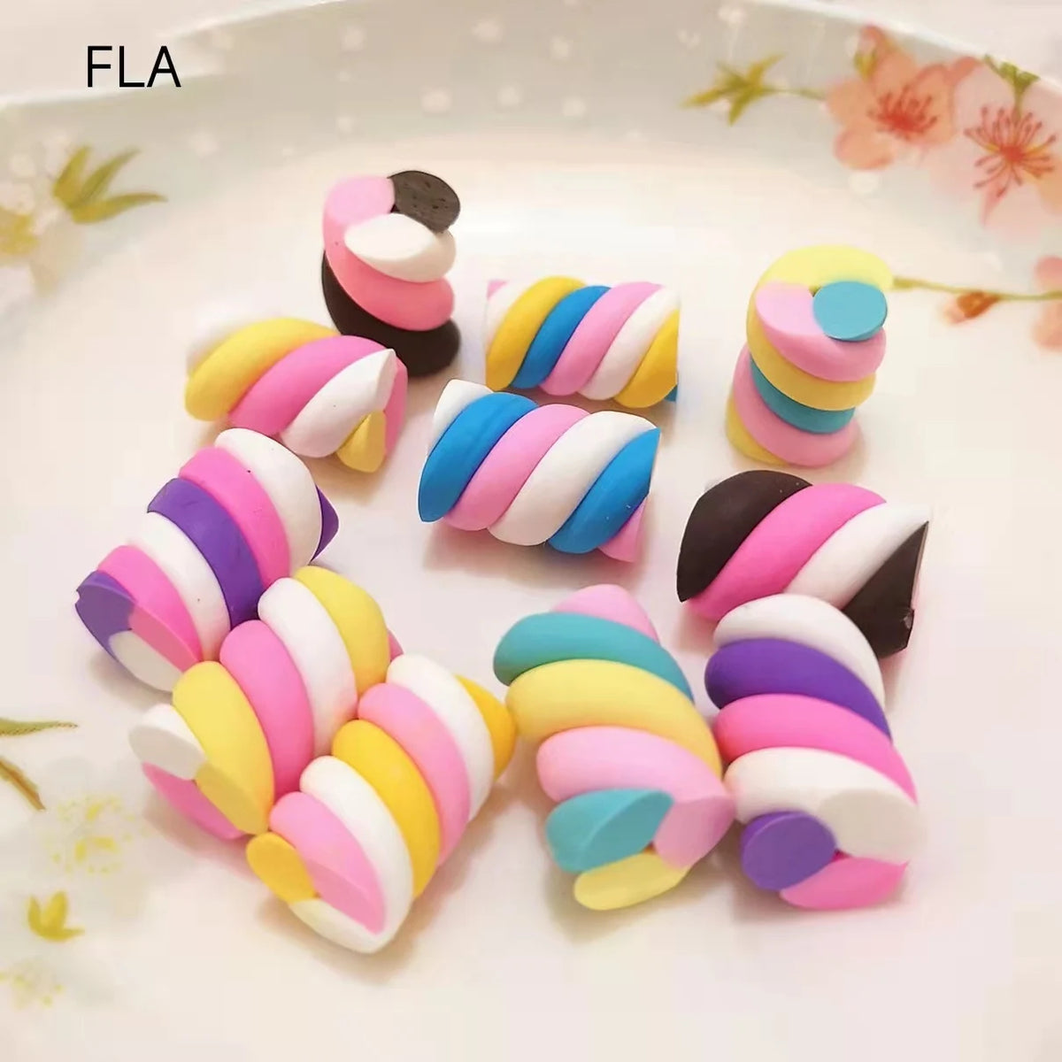 A collection of ten colorful polymer clay marshmallow charms in various striped and solid colors arranged on a white plate.