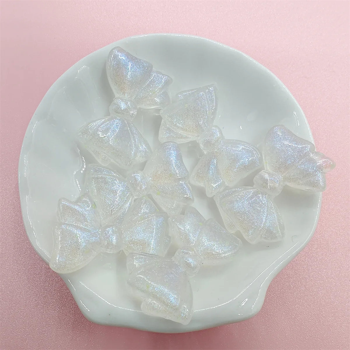 Clear iridescent mermaid bowknot beads arranged on a white dish for jewelry making