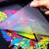 A hand holds a transparent heat transfer patch featuring vibrant, colorful abstract designs on a dark background.