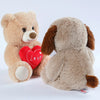 A light brown plush bear and a tan dog plush toy with a red heart print on the bear's chest.