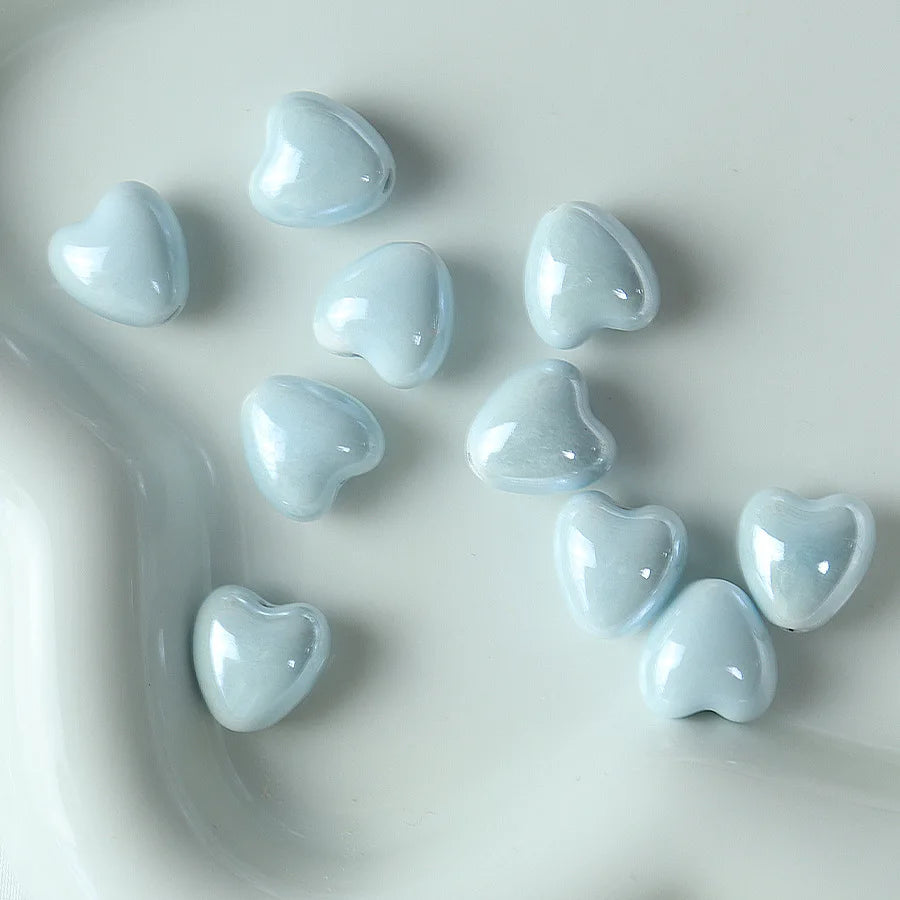 A collection of light blue heart-shaped ceramic beads scattered on a white surface.