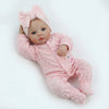 A lifelike soft body baby doll with pink hair bow and pink fuzzy clothing lying on a white background.
