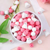 A bowl filled with pink and white silicone beads shaped like ghosts and flowers for jewelry and crafting.