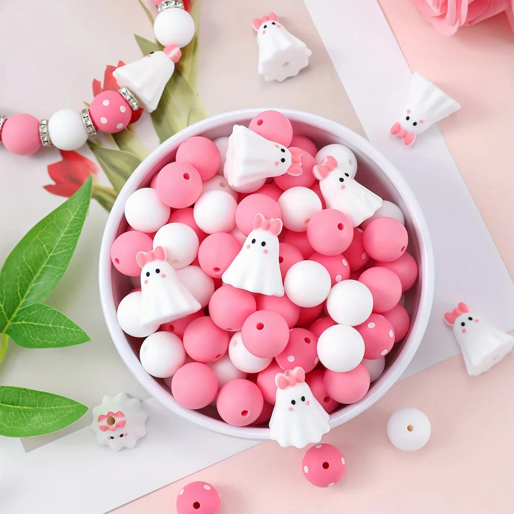 A bowl filled with pink and white silicone beads shaped like ghosts and flowers for jewelry and crafting.