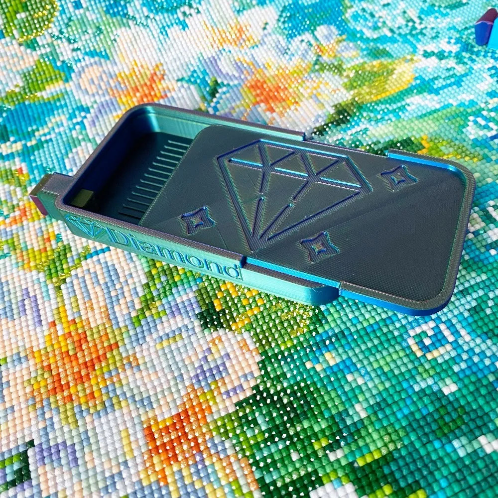A rectangular plastic tray organizer for diamond painting supplies resting on a colorful, textured surface.