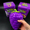 A hand holds a purple squishy grape toy next to its packaging box.