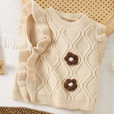 A beige knit sweater vest for girls featuring a diamond pattern and small flower-shaped appliqués.
