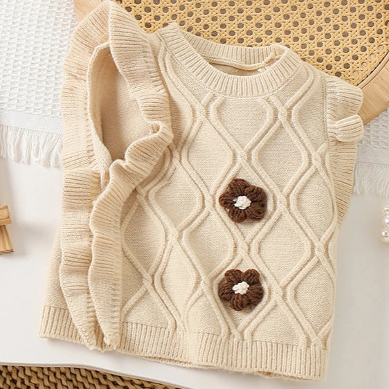 A beige knit sweater vest for girls featuring a diamond pattern and small flower-shaped appliqués.
