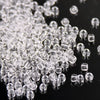 A close-up view of clear glass rice beads scattered on a dark surface.