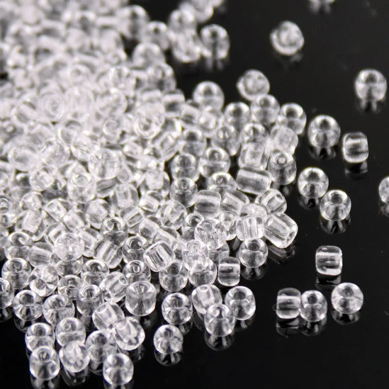 A close-up view of clear glass rice beads scattered on a dark surface.