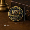 A round brass lapel pin featuring an eagle and the text America 1776-2026 surrounded by stars.