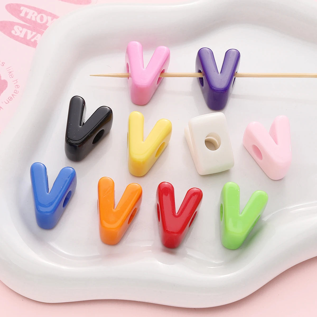 A collection of colorful acrylic letter beads shaped like the letter V arranged on a white tray.