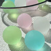A collection of round squishy toys in pastel shades including green, pink, and light blue resting on a white textured surface
