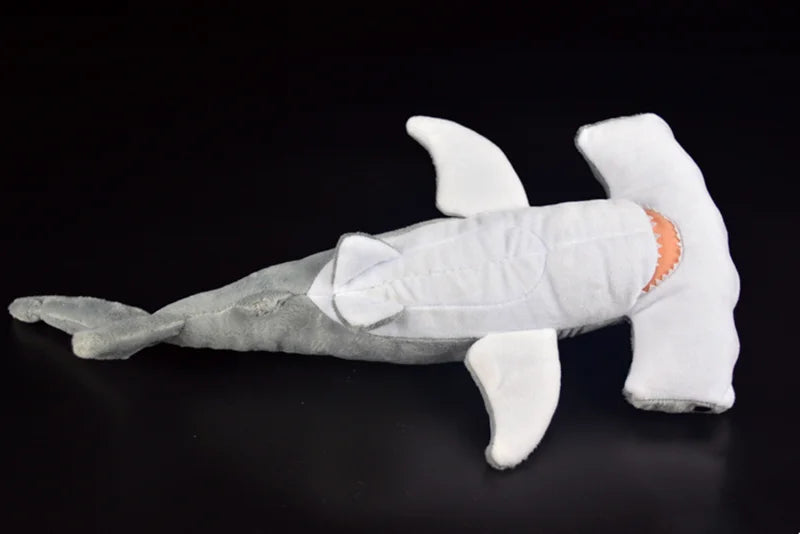 A white and gray plush toy of a hammerhead shark with fins and a tail.