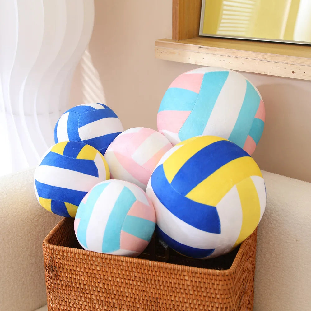 A collection of colorful, striped soft plush volleyball pillows in blue, pink, and yellow are displayed in a woven basket.