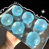 A hand holds a clear container filled with light blue squeezable soft fidget balls for stress relief.