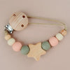 A wooden pacifier clip with silicone beads and a cord, featuring a star-shaped bead.