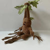 A brown mandrake plush toy with green leaves, sitting on a white surface.