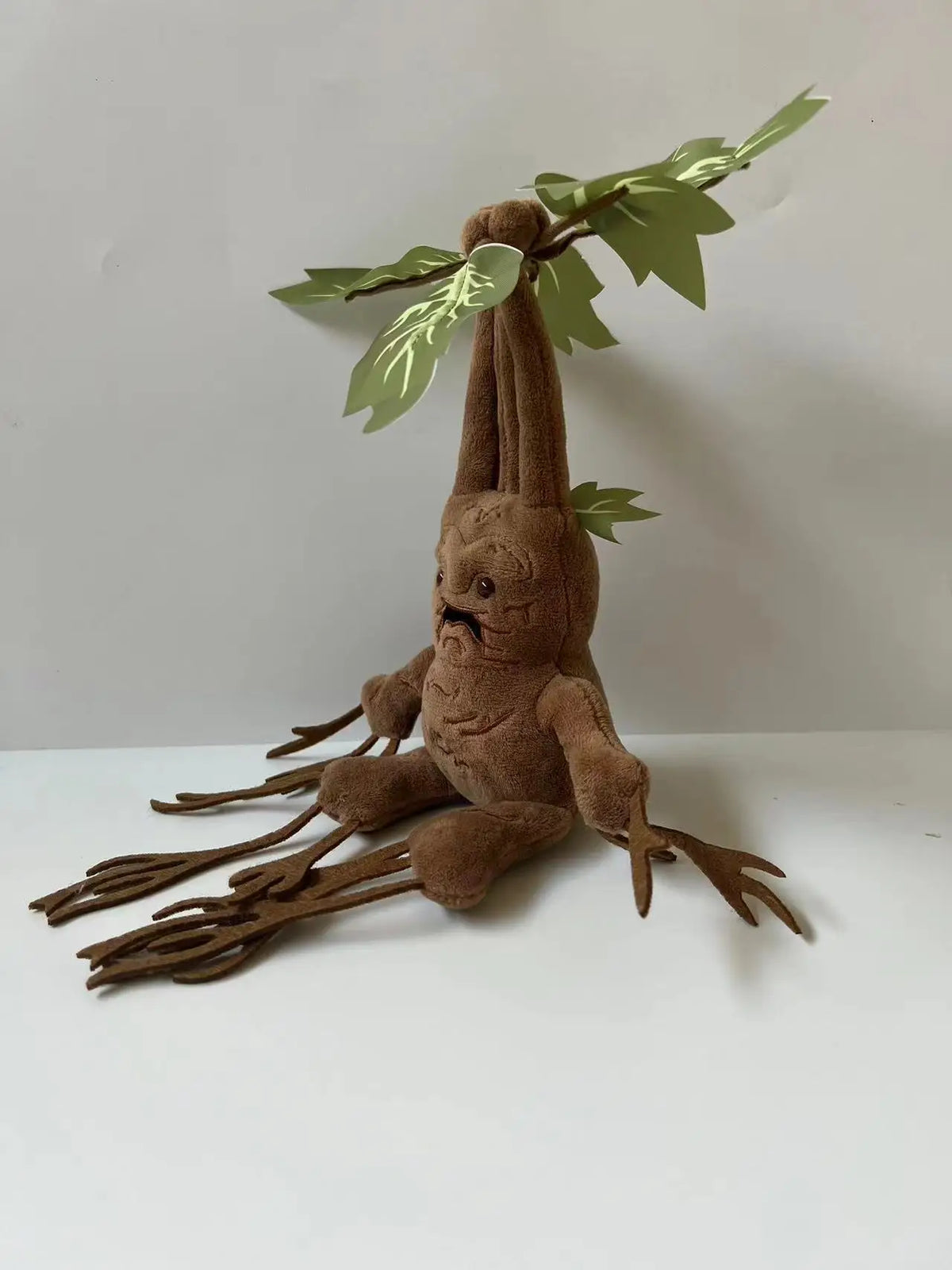 A brown mandrake plush toy with green leaves, sitting on a white surface.