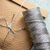 A spool of metallic silver yarn or glitter thread resting on brown kraft paper.
