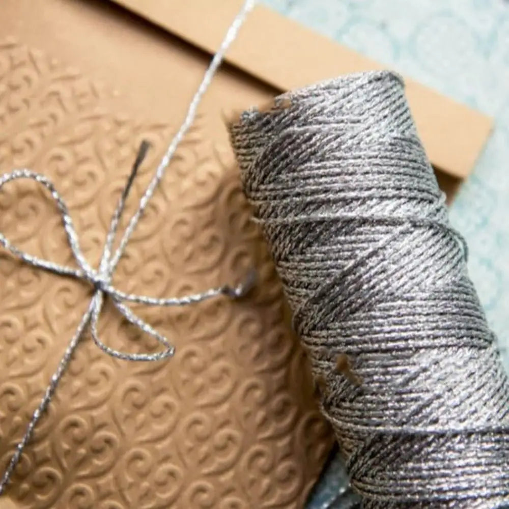 A spool of metallic silver yarn or glitter thread resting on brown kraft paper.