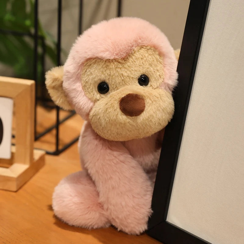 A pink plush monkey soft toy with light brown accents sitting next to a black frame.