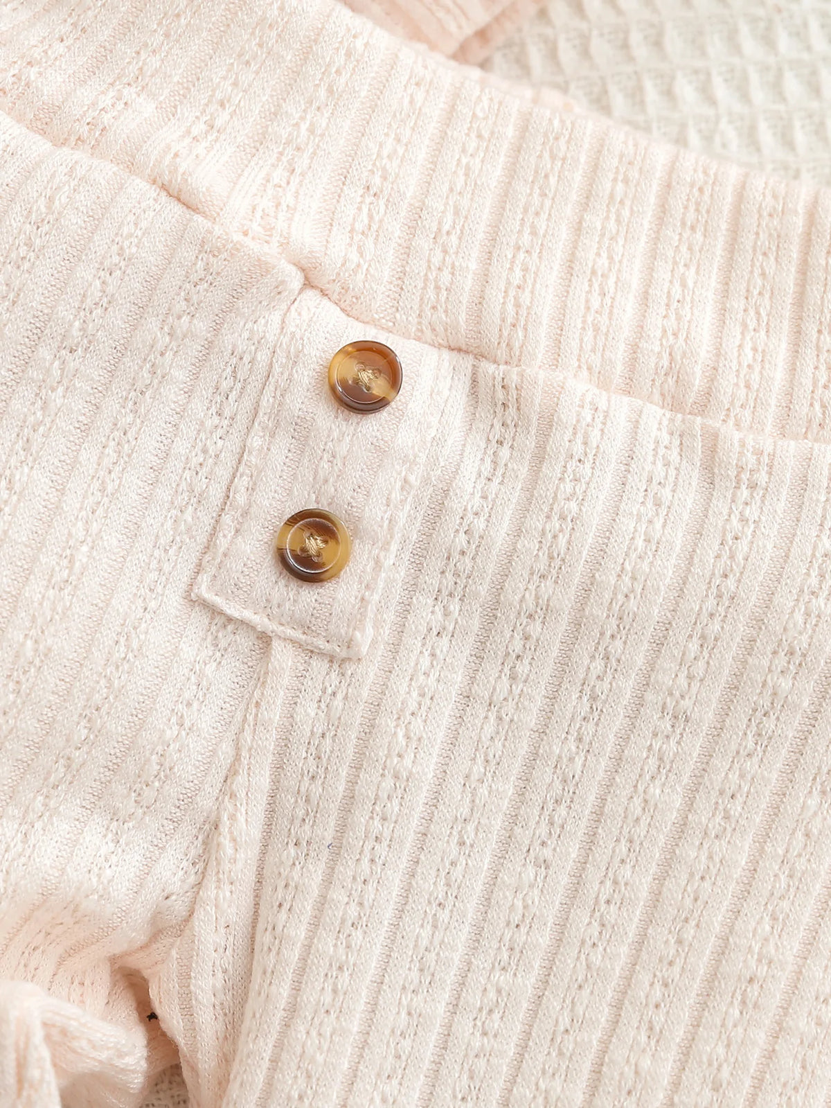 Close-up of a light pink knitted baby romper and pants set with wooden buttons.