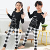 Two children wearing black long-sleeved tops and checkered pants with an astronaut print