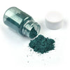 A glass jar of teal green mica powder next to a spilled pile of the same powder and a white lid.