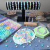 A display of various frosted golden foil acrylic beads in pastel colors and shades, some arranged on a wooden stand.