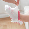 A close-up of a white cotton sock with a pink cartoon rabbit design and non-slip grips on a foot.