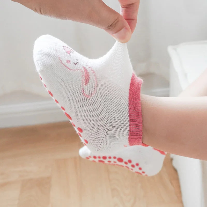 A close-up of a white cotton sock with a pink cartoon rabbit design and non-slip grips on a foot.
