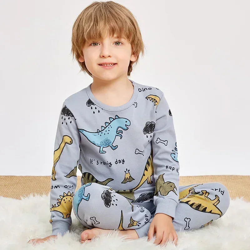 A young boy wearing a light blue long-sleeved pajama set with an astronaut print, sitting on a white fluffy surface.