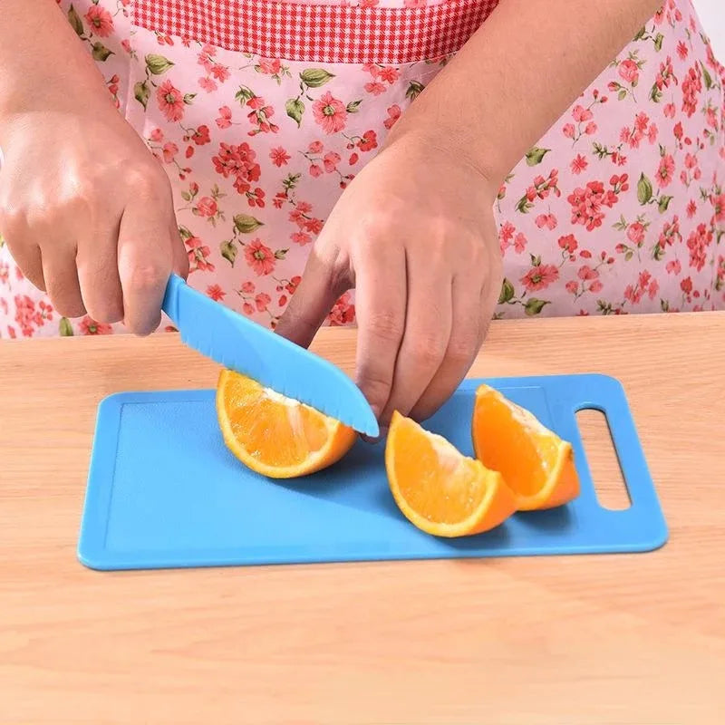Hands are using a blue plastic safety knife to cut an orange on a blue cutting board.