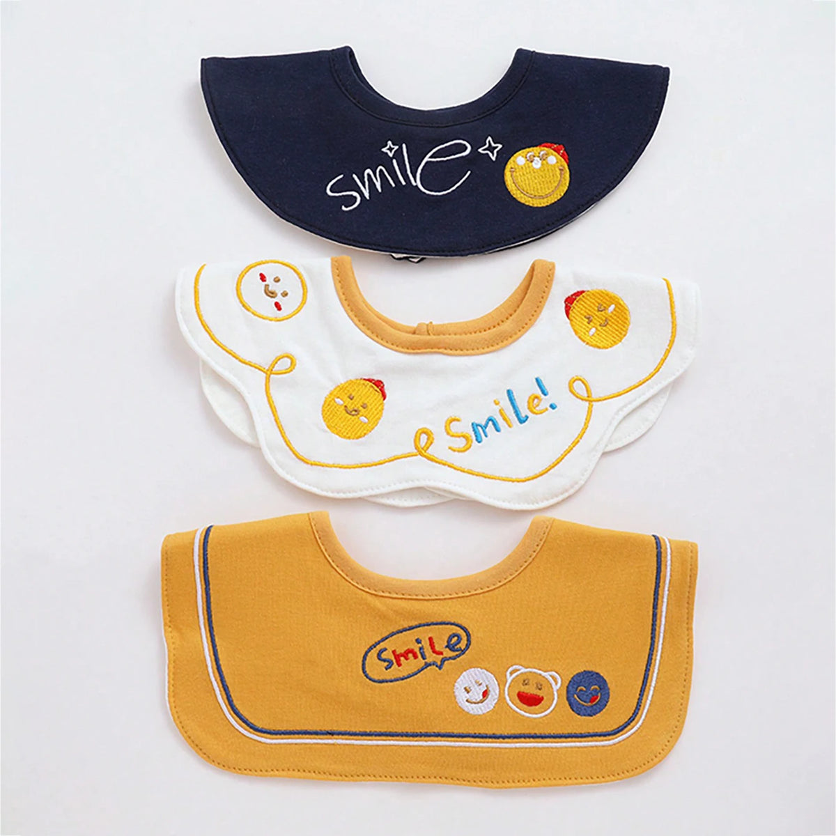 A set of three yellow and navy baby waterproof drool bibs with smiling face designs