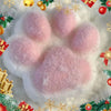 A giant pink fluffy cat paw squishy toy surrounded by festive holiday decorations.