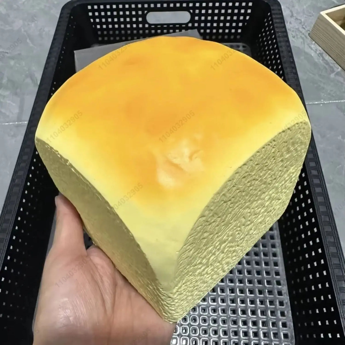 A yellow and orange squishy toy shaped like a loaf of bread is held in a hand inside a black mesh basket.