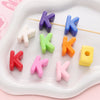 A collection of colorful acrylic letter beads in various shades like purple, blue, green, orange, and pink arranged on a whit