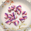 A collection of pink and purple striped polymer clay marshmallow charms arranged on a white plate.