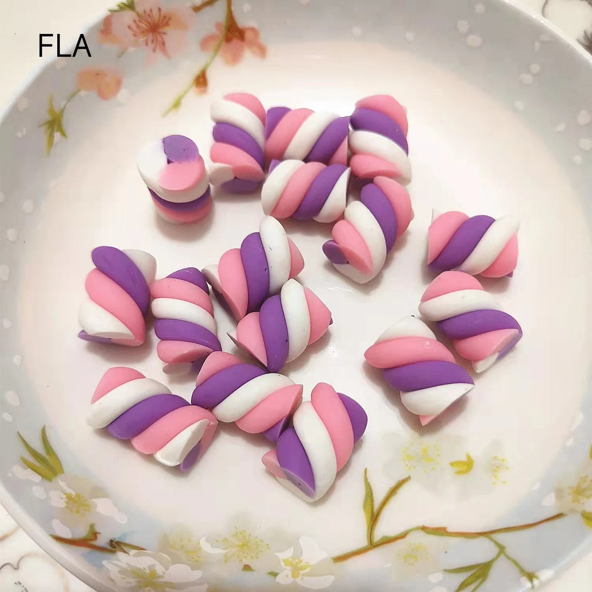 A collection of pink and purple striped polymer clay marshmallow charms arranged on a white plate.