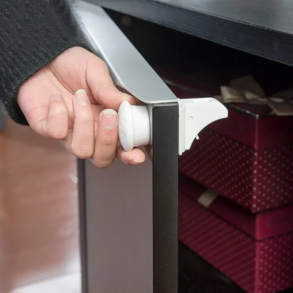 Eine Hand öffnet eine magnetische Schließvorrichtung für Kindersicherheit an einem dunklen Schrank.