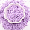 Purple polymer clay slice sprinkles scattered on a white background, with some forming a decorative mound.
