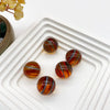 Collection de billes en verre rond et brillant avec des tons ambre et orange, arrangées sur un plateau blanc.