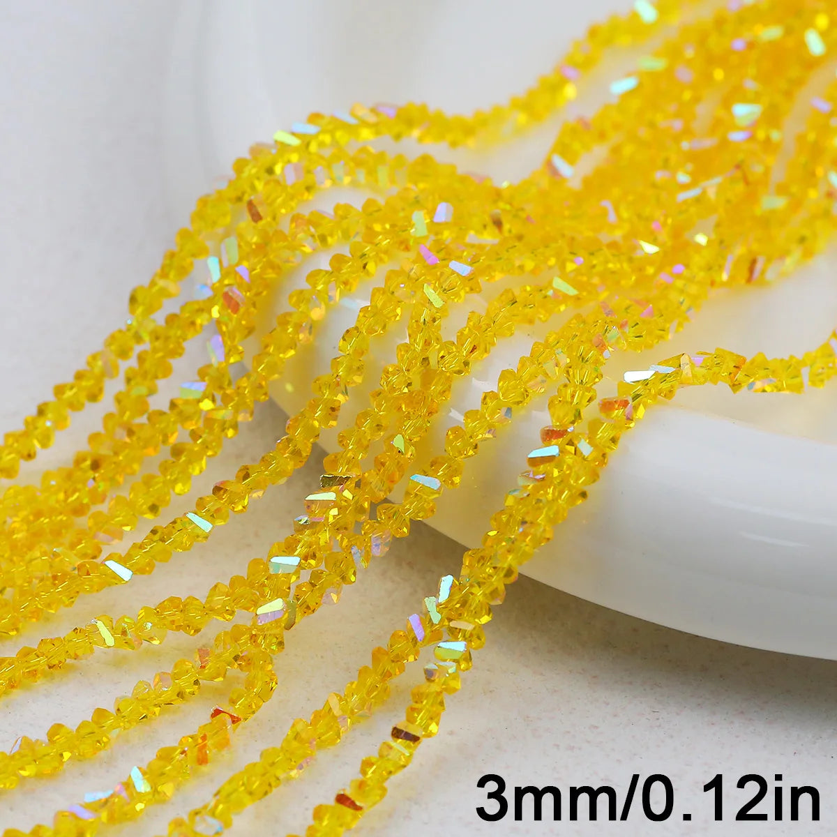 Yellow crystal triangle beads strung on a string and displayed next to a white object.