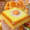 A hand holds a yellow squishy fried egg toast stress relief toy next to a loaf of bread.